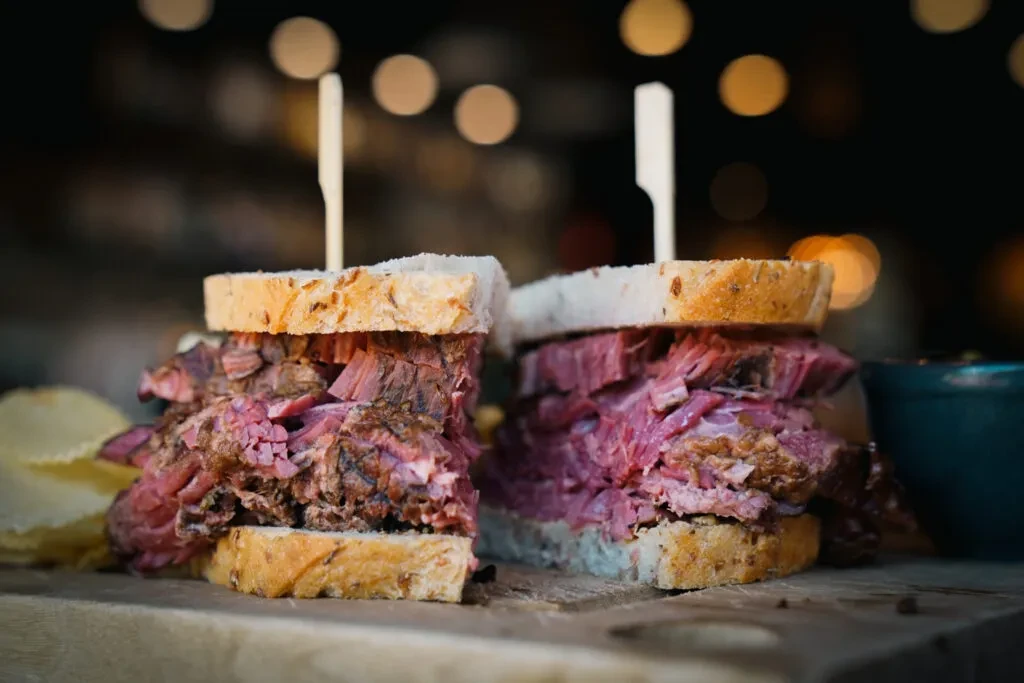 Deli pastrami sandwiches with seeded bread, skewers, and chips.