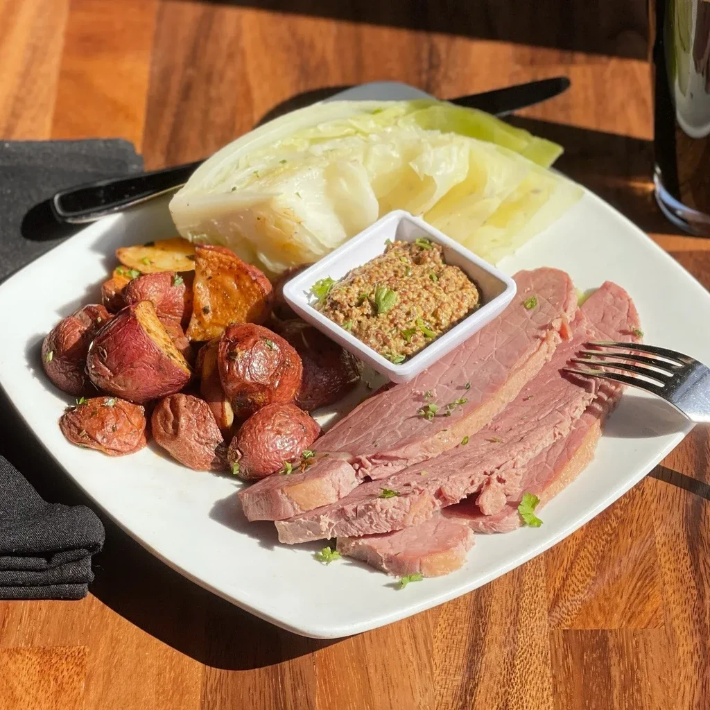 A plate of corned beef, roasted potatoes, cabbage, and mustard.