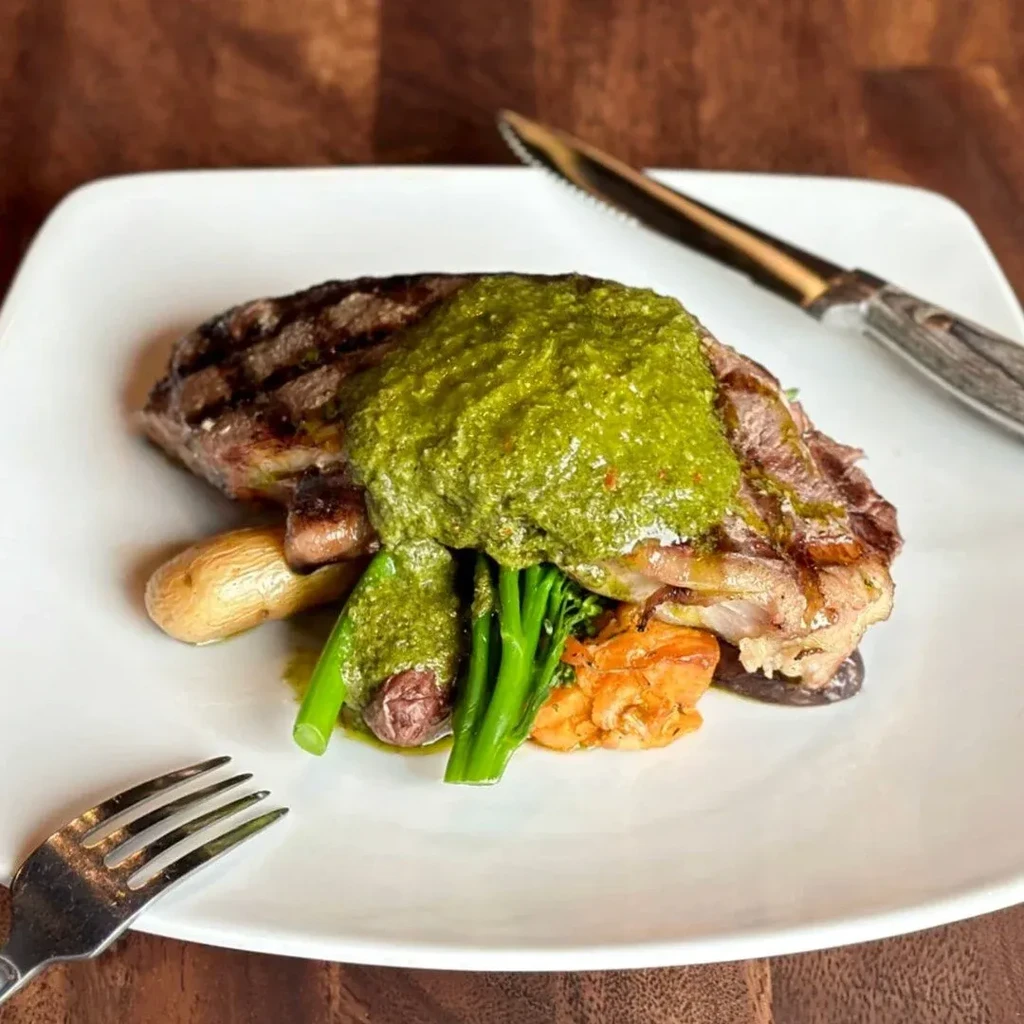 Grilled steak with green sauce, broccolini, potatoes, and roasted orange vegetables.
