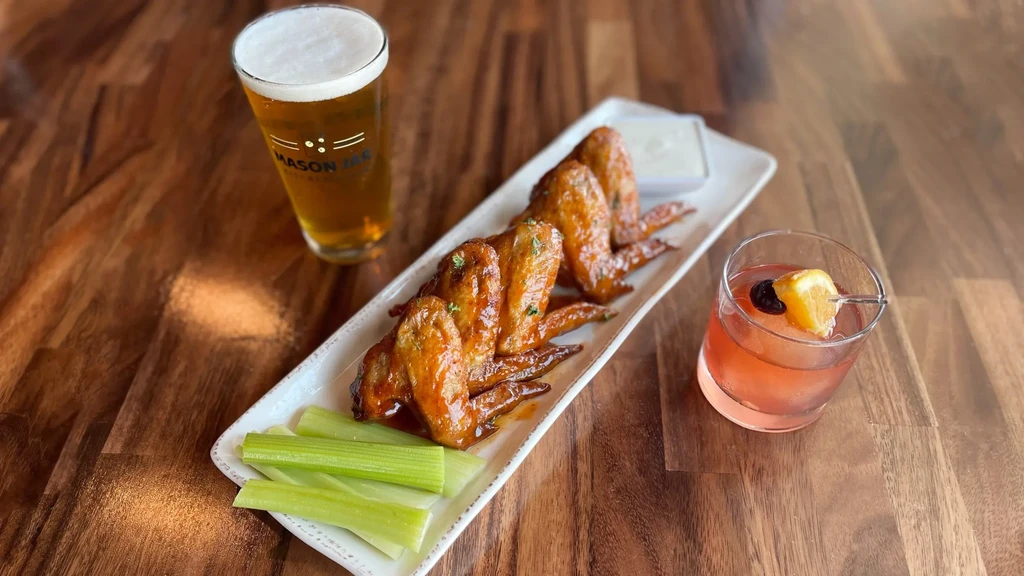 Plate of chicken wings, celery, sauce, beer, and a cocktail.