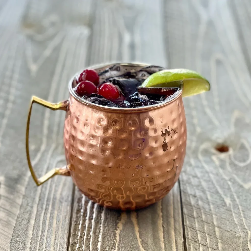 Hammered copper mug with dark drink, cranberries, and lime garnish.