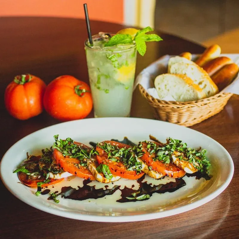 Fresh Caprese salad, cocktail, and bread on a dark wooden table.