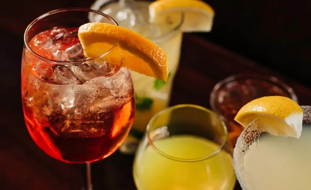 Close-up of several colorful cocktails with fruit garnishes on a dark surface.
