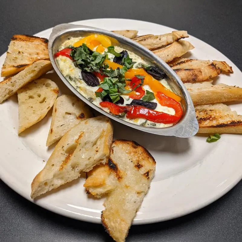 Creamy baked dip with peppers, olives, basil, served with toasted bread.
