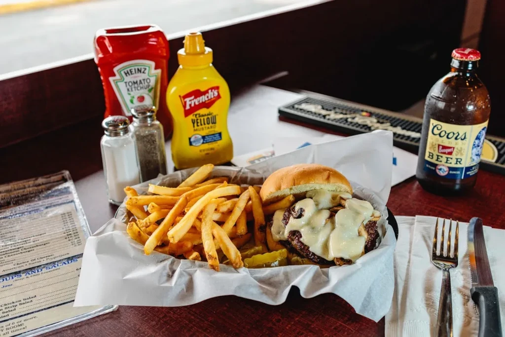 Cheeseburger and fries with beer and condiments on a wooden table.