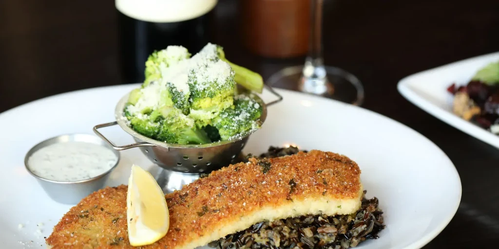Plated breaded fish, wild rice, broccoli, creamy sauce, and lemon.