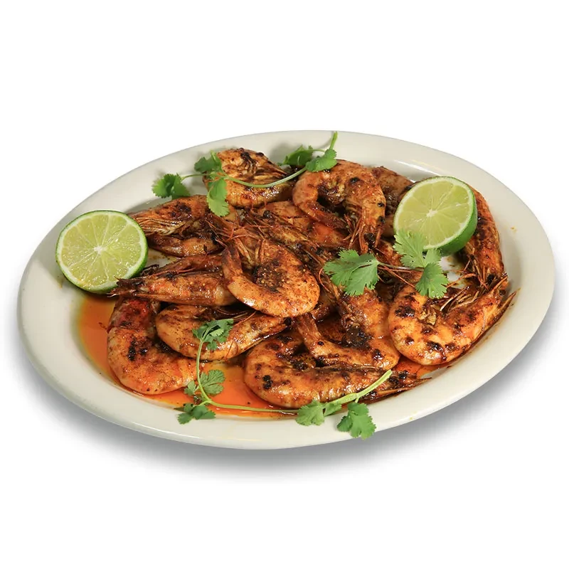 White plate with grilled shrimp, cilantro, lime wedges, and sauce.