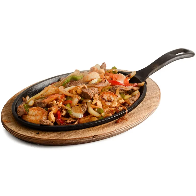Sizzling shrimp and beef fajitas in skillet on wooden board.