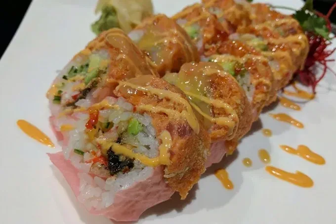 Crispy sushi rolls with yellow and orange sauces on a white plate.