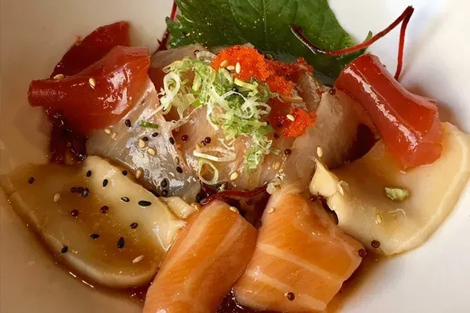 Overhead view of colorful sashimi or ceviche, with fish, roe, and herbs.