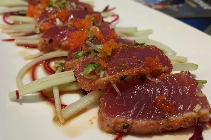Seared tuna tataki with roe, herbs, and vegetables on a white plate.