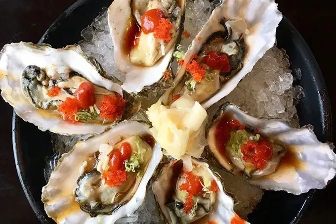 Six garnished oysters with roe, herbs, and ginger on crushed ice.