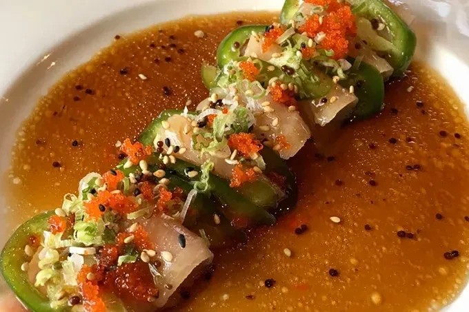 Four raw whitefish and jalapeño appetizers with roe, scallions, and sauce.