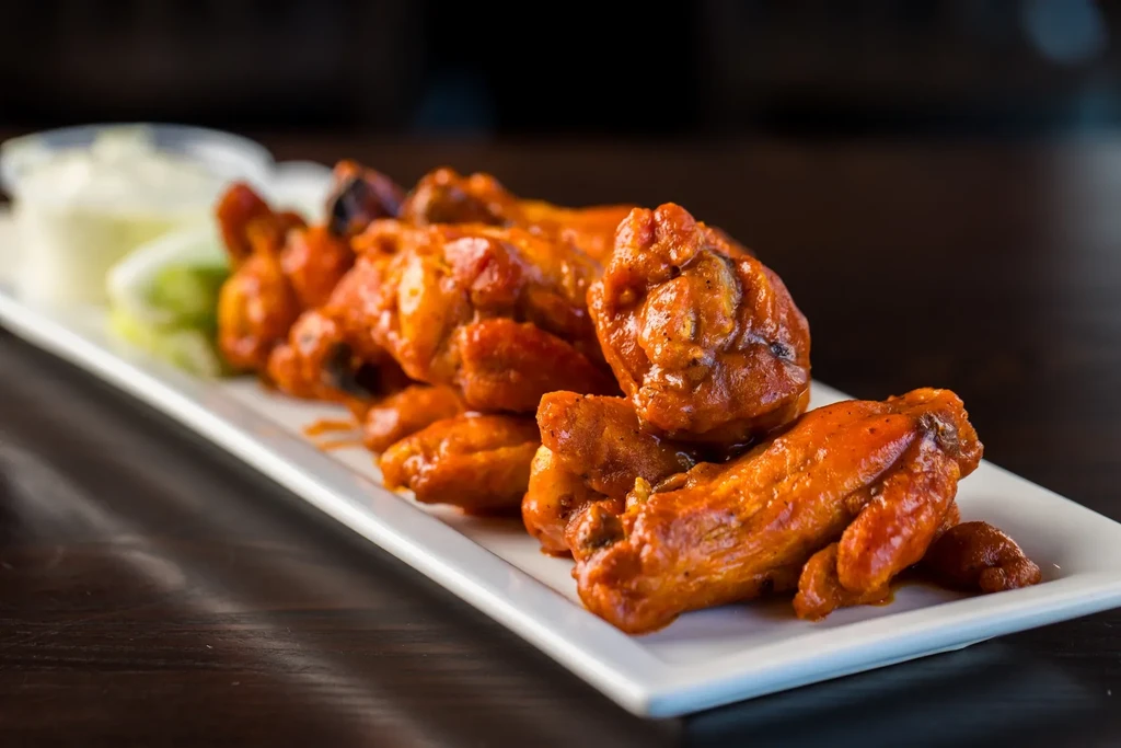 Glossy buffalo wings on a white plate with dipping sauce and celery.