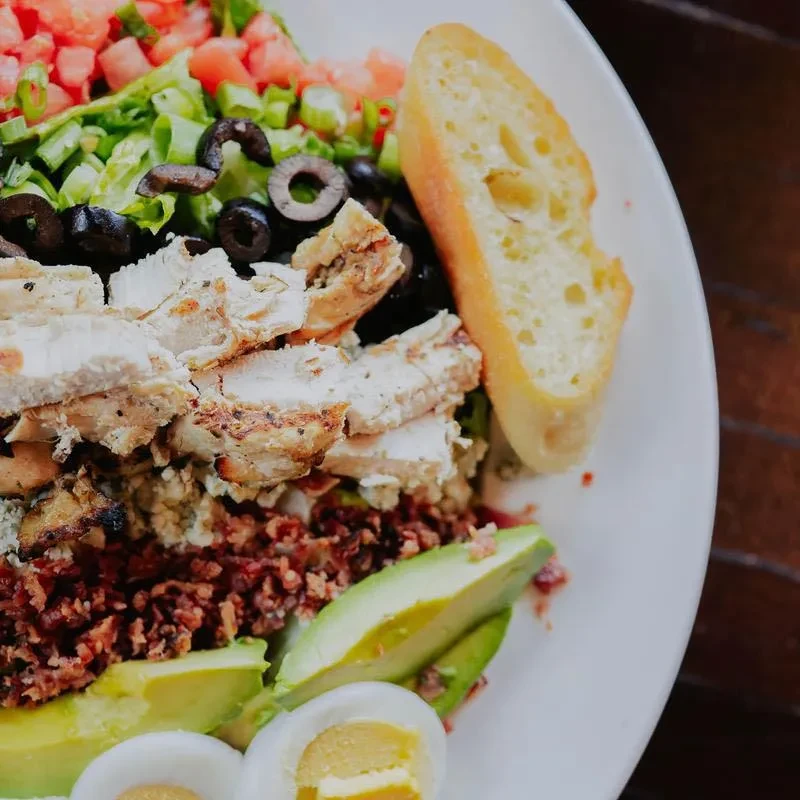 Close-up of a colorful Cobb salad with chicken, avocado, egg, and baguette.