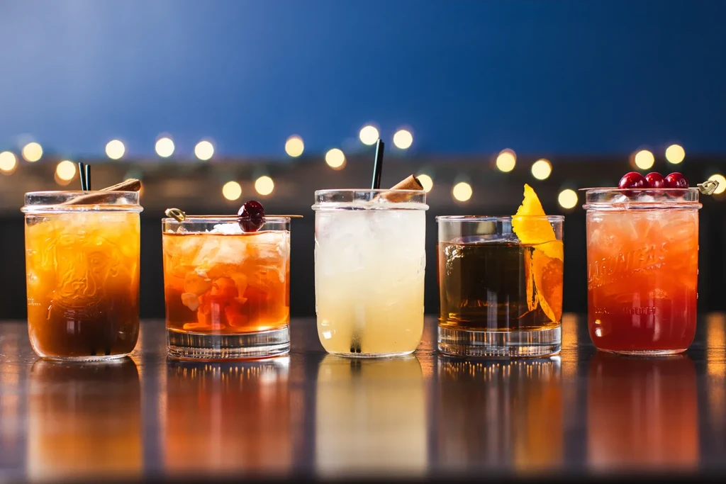Five distinct cocktails in a row, with ice, garnishes, and reflections.