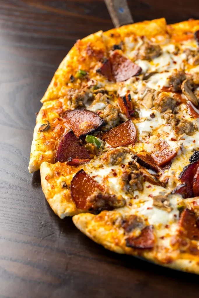 Close-up of bubbling pizza with pepperoni, sausage, mushrooms, green peppers.