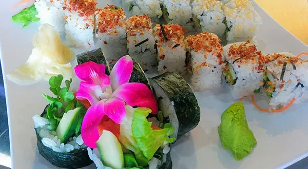 Platter of diverse sushi rolls with pink orchid, ginger, and wasabi.