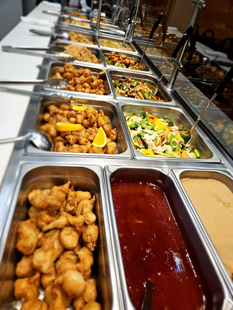 Buffet line displaying chicken, noodles, stir-fry, and sauces in chafing dishes.