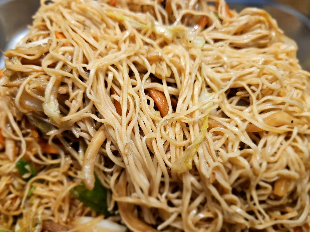 Close-up of tangled saucy stir-fried noodles with cabbage and carrots.
