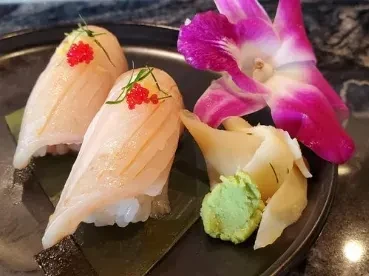Two nigiri sushi, red roe, wasabi, ginger, and a purple orchid.