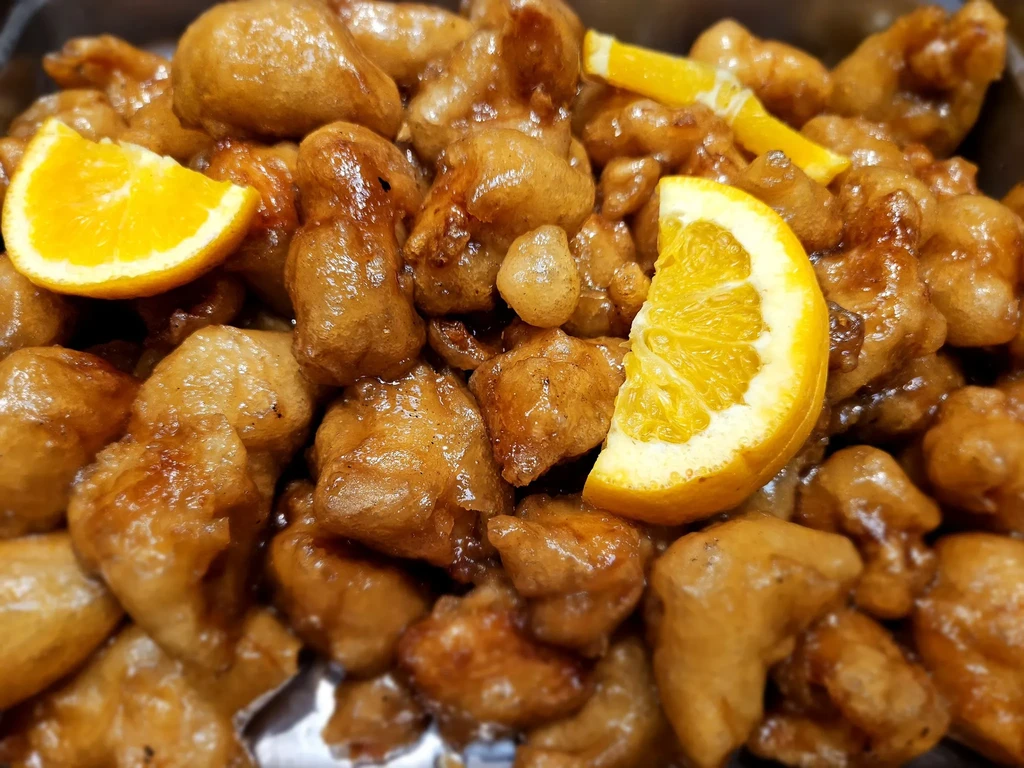 Close-up of glazed orange chicken with two orange slices.