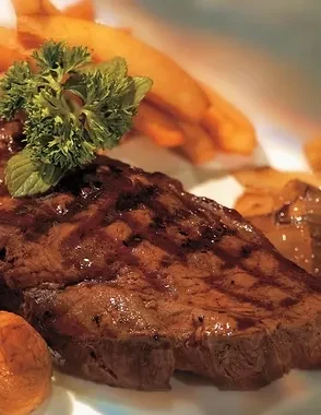 Grilled steak on white plate with herbs and blurred french fries.