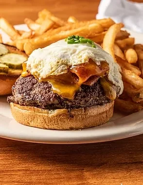 Beef burger with cheese, bacon, fried egg, chives, and fries.