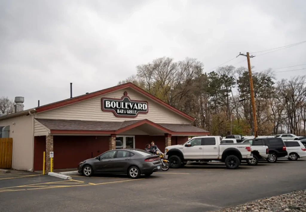 Wide shot of Boulevard Bar & Grille, light facade, parked cars.