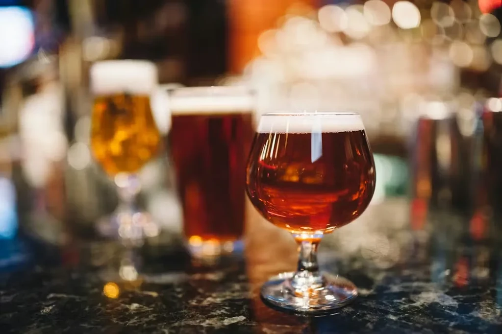 Three glasses of amber, golden, and dark beer on a bar.