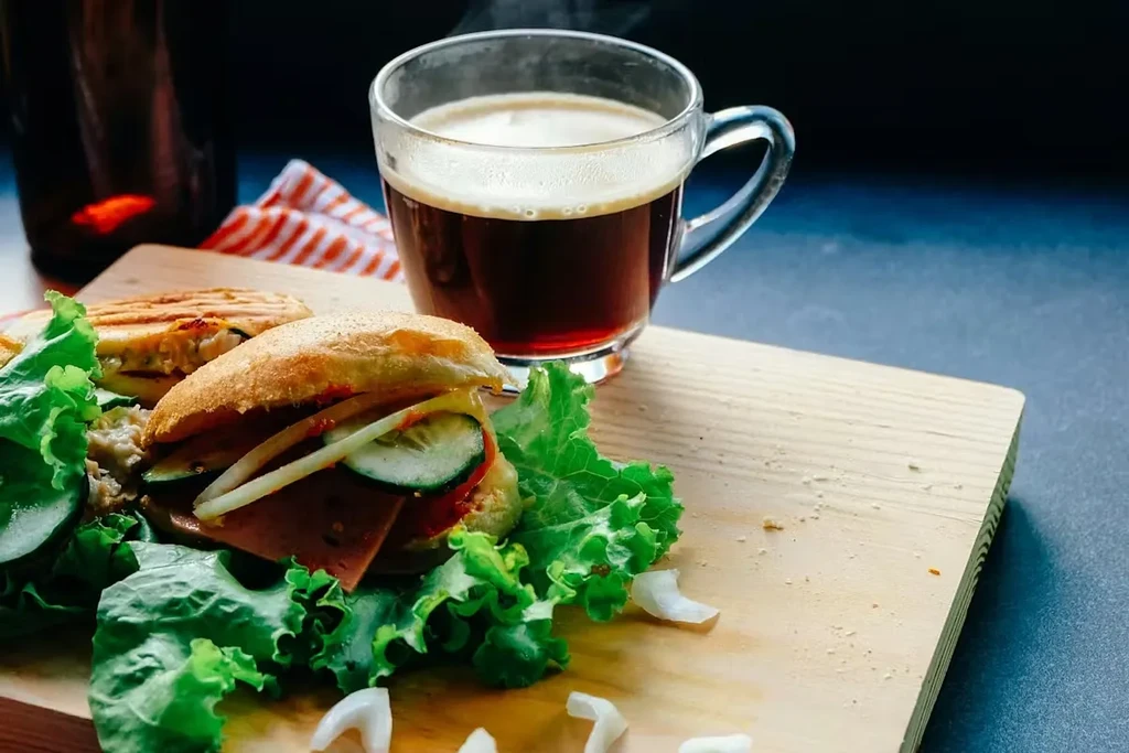 Close-up of a sandwich, panini, and hot coffee on a wooden board.