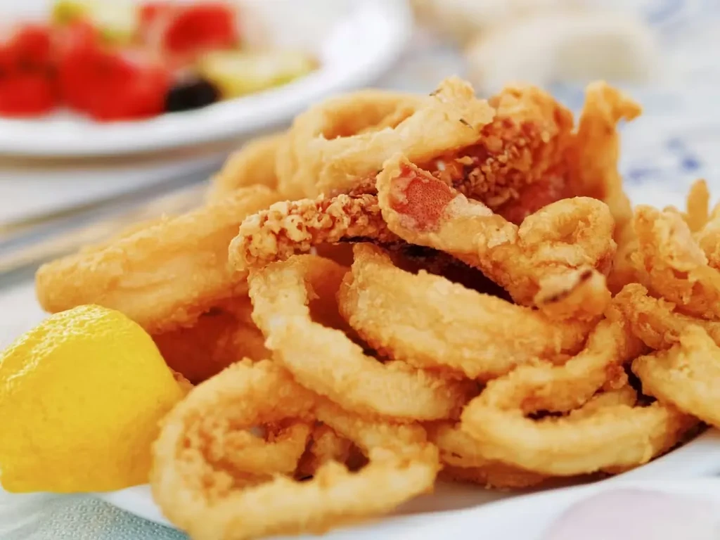 Crispy fried calamari rings piled high on a white plate with lemon.