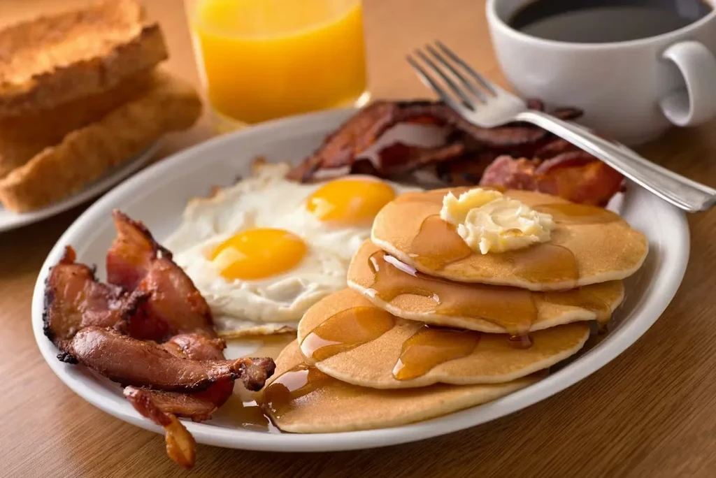 Full breakfast plate with pancakes, sunny-side eggs, and crispy bacon.