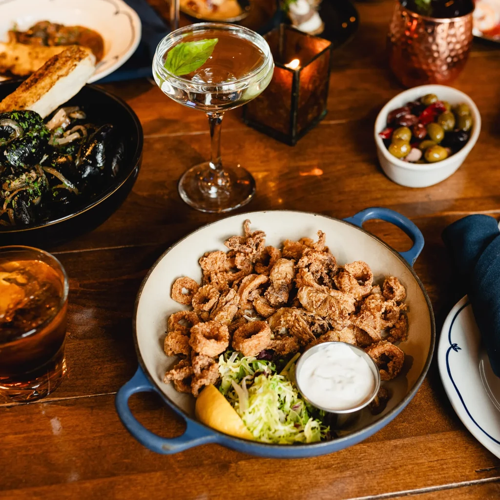 Wooden table with fried calamari, mussels, drinks, and a lit candle.