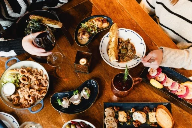 Top-down view: people dining at a wooden table with diverse dishes.