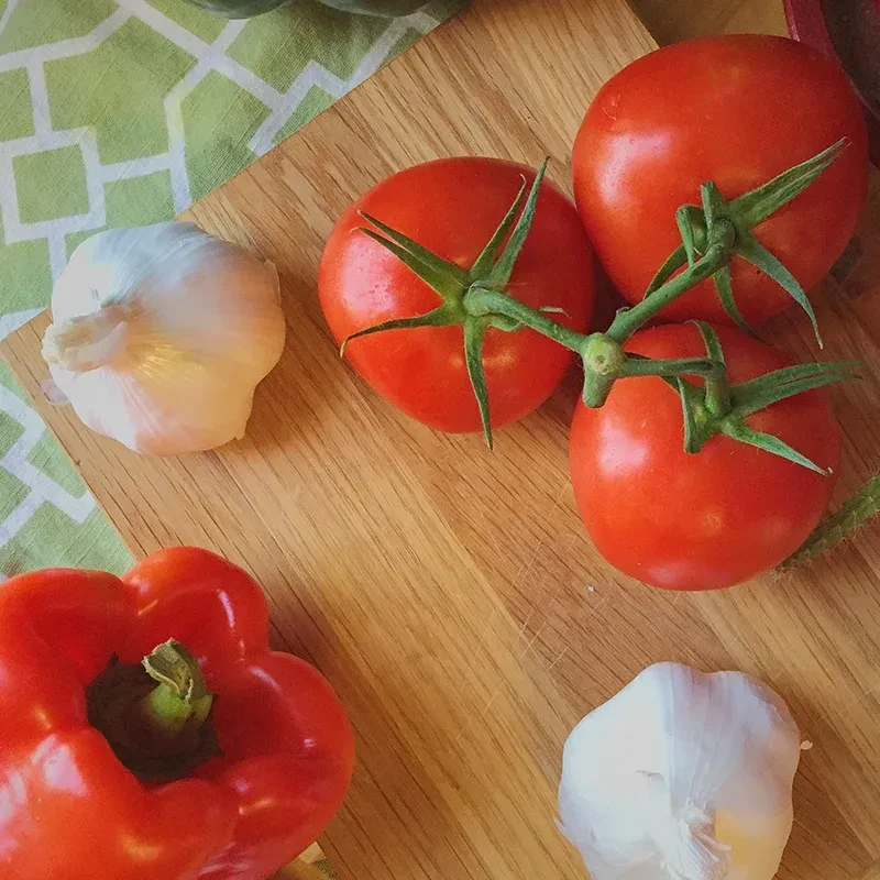 Fresh tomatoes on vine, garlic, and bell pepper on a wooden board.