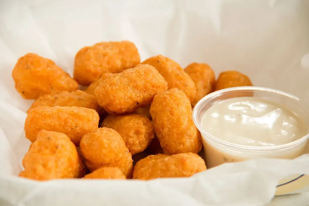 A container of crispy tater tots with creamy herb dipping sauce.