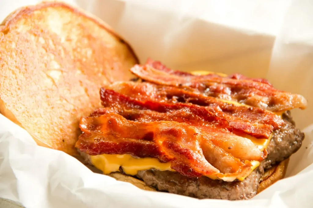 Close-up of a bacon double cheeseburger in a white wrapper.
