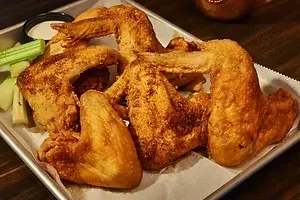 Crispy golden-brown chicken wings, celery, and creamy dip on metal tray.