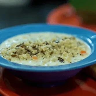 Close-up of creamy wild rice and carrot soup in a blue bowl.