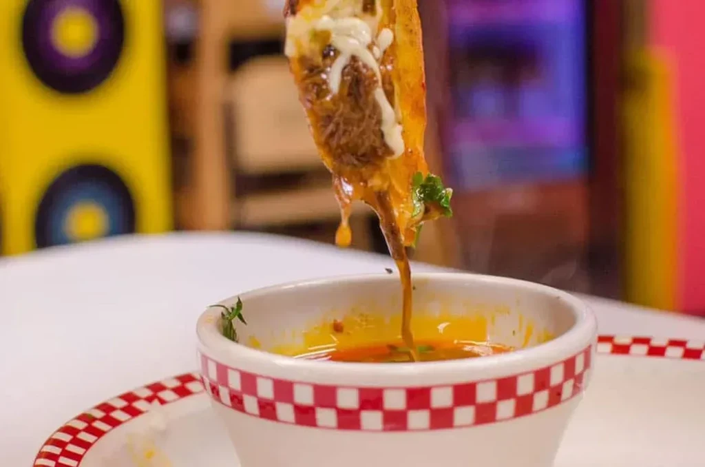 Birria taco with melted cheese and shredded meat dipped into consommé.