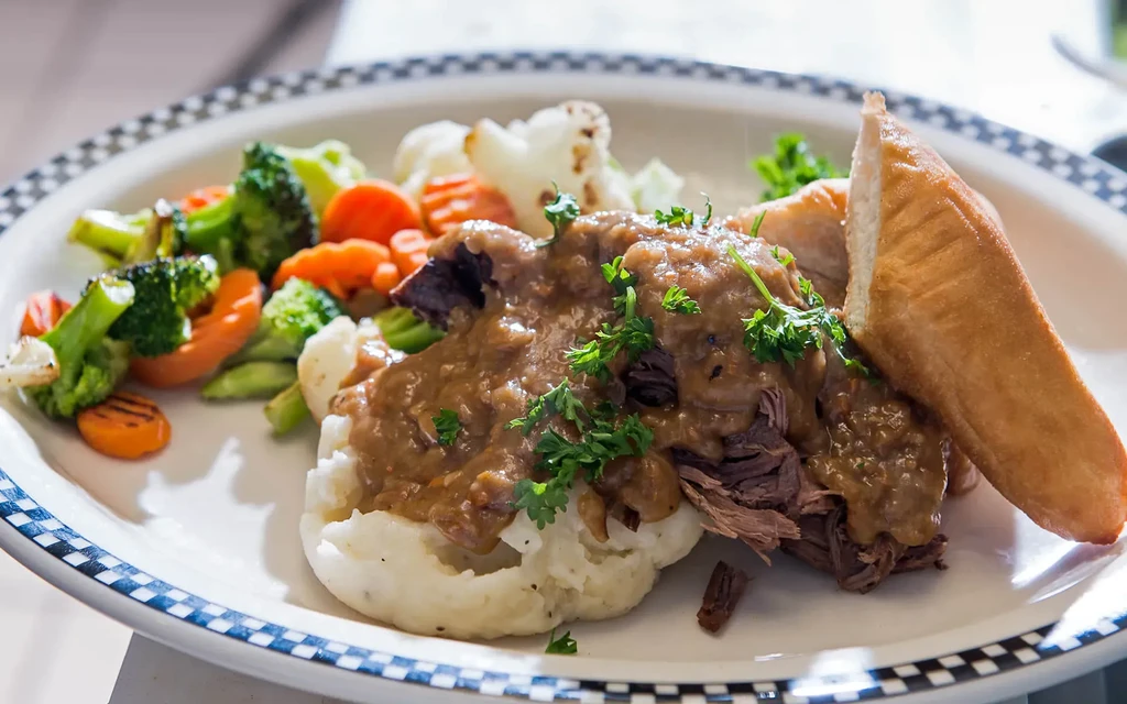 Mashed potatoes with shredded meat and gravy, vegetables, and bread.