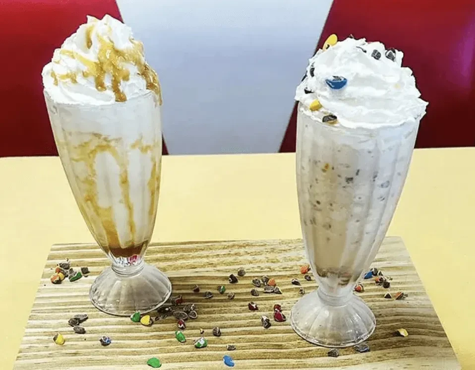 Two whipped cream-topped milkshakes, caramel and cookies-and-cream, with candy.