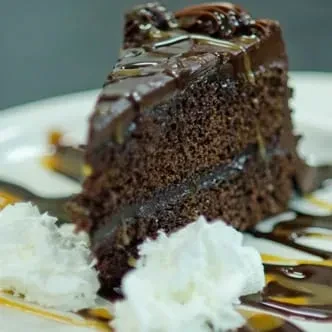 Close-up slice of chocolate cake with ganache, caramel, and whipped cream.