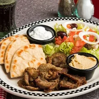 Mediterranean plate with grilled meat, pita, salad, tzatziki, and hummus.