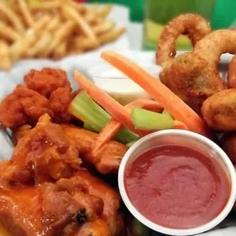 Close-up of buffalo wings, celery, carrots, fries, and onion rings.