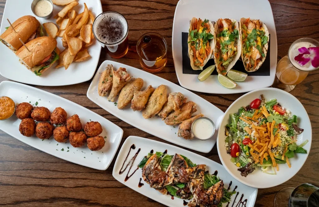 Assortment of sandwiches, tacos, wings, salad, and cocktails on a table.