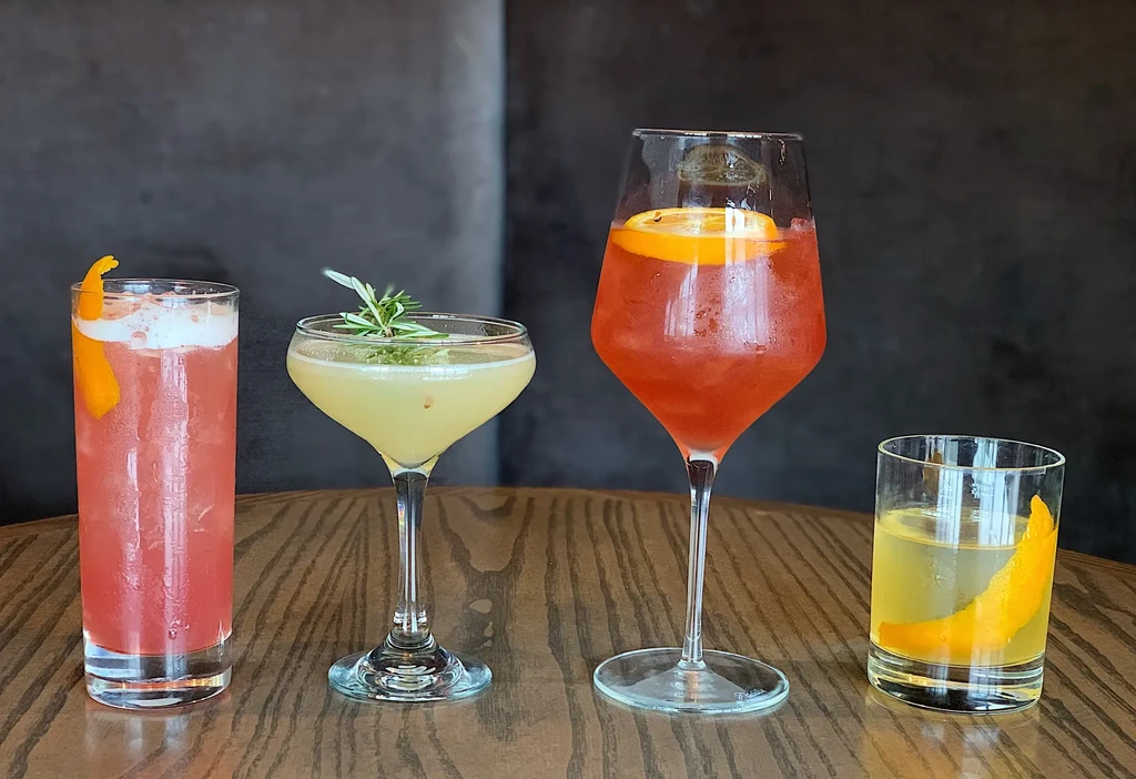 Four cold, colorful, garnished cocktails in various glasses on wood.
