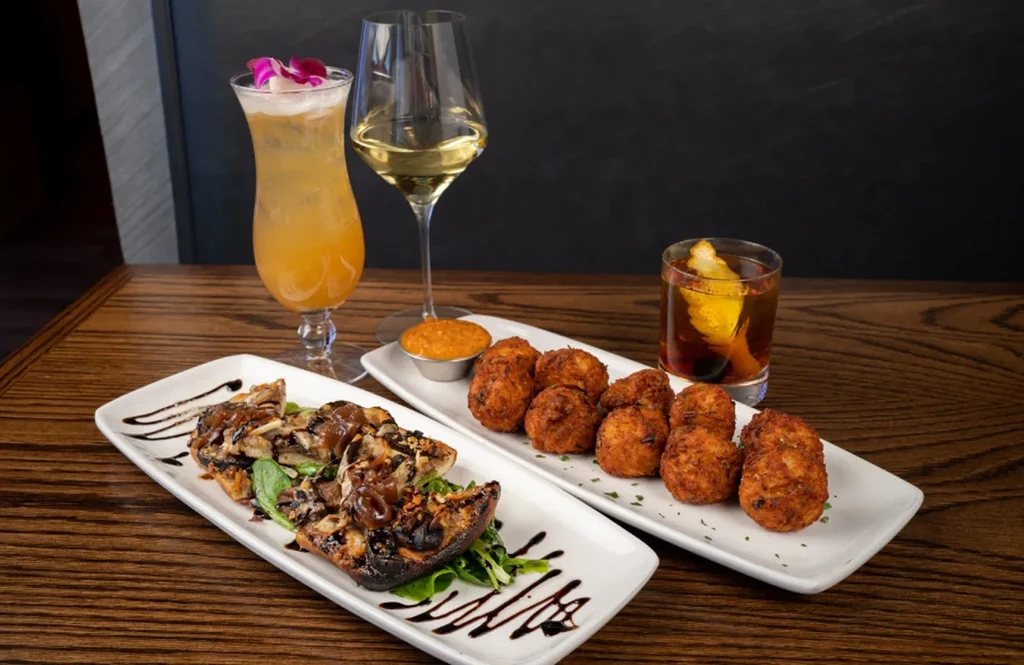 Grilled portobello, fried items, and three drinks on a dark table.
