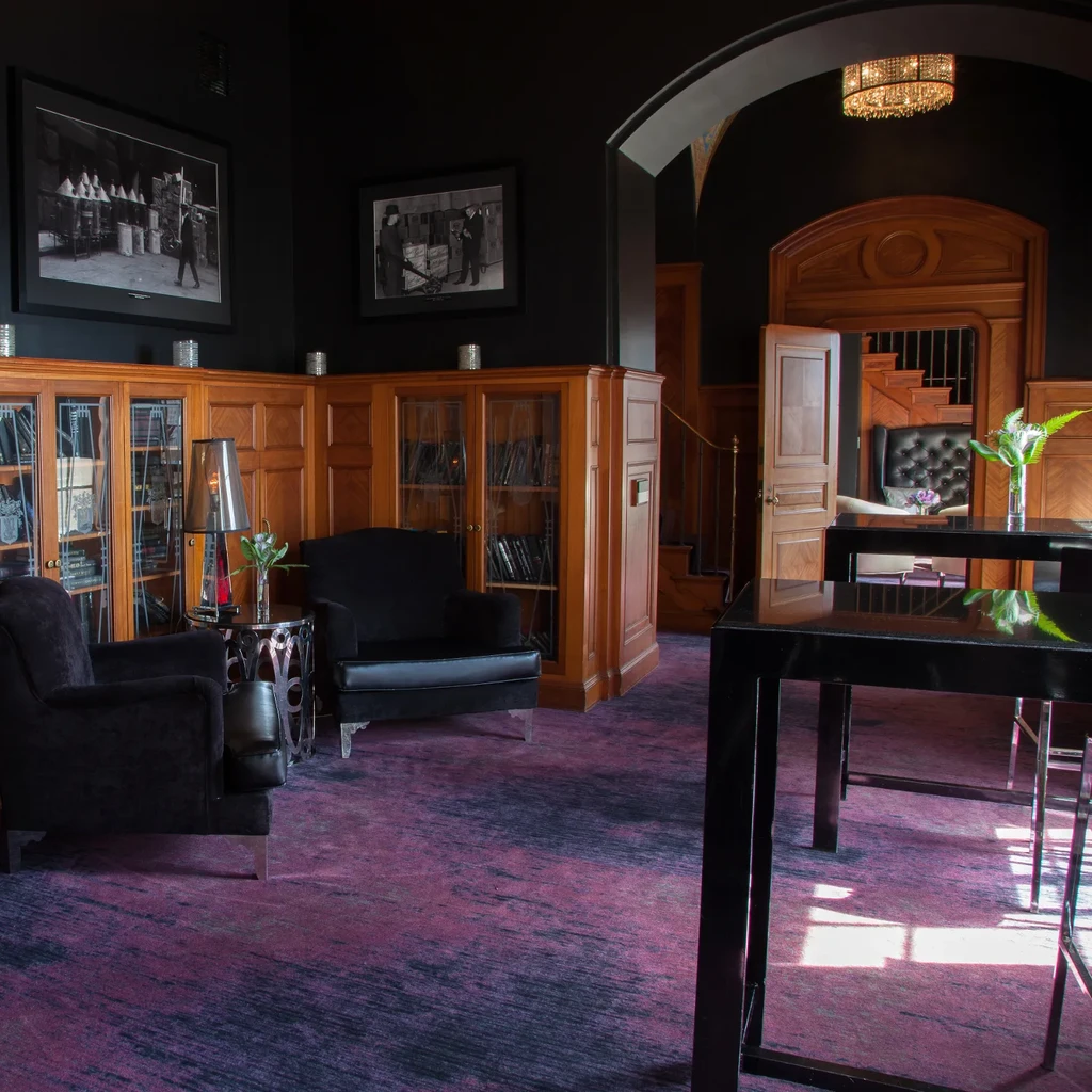 Dimly lit luxury lounge with dark walls, armchairs, wood cabinetry.